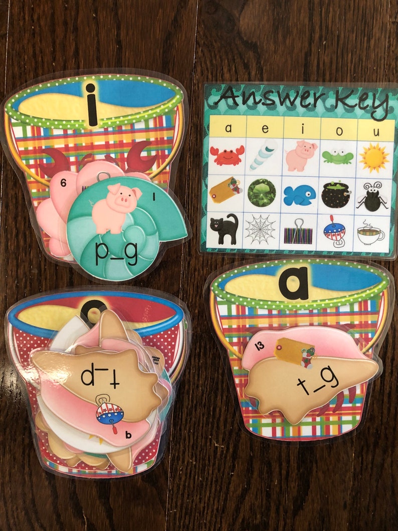 Pu&ograve; includere: Un set di quattro secchielli di plastica colorati con lettere e immagini all'interno. I secchielli sono decorati con motivi a scacchi rossi e bianchi. Le lettere sono "i", "a", "d", e "t". Le immagini includono un maiale, un granchio, una conchiglia e un pesce. I secchielli fanno parte di un gioco di apprendimento per bambini. La chiave di risposta &egrave; anche inclusa, mostrando la lettera corretta per ogni immagine.