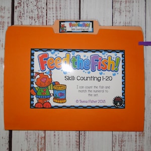 May include: An orange file folder labelled Feed the Fish! Skill Counting 1-20. The front features a cartoon cat holding a fish food container, with text stating I can count the fish and match the numeral to the set, and Teena Fisher 2018.