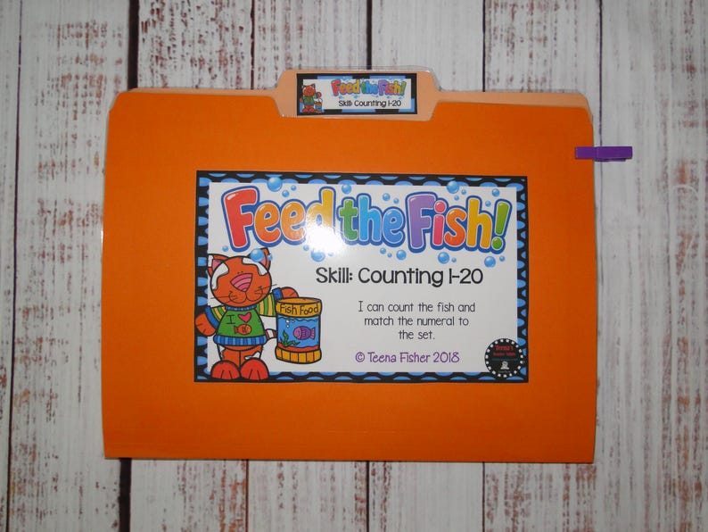 May include: An orange file folder labelled Feed the Fish! Skill Counting 1-20. The front features a cartoon cat holding a fish food container, with text stating I can count the fish and match the numeral to the set, and Teena Fisher 2018.