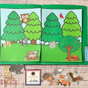 May include: A green folder with a woodland scene featuring cartoon trees, animals, and the text "I can put animals in the woodlands." Includes animal cutouts like a bear, fox, and owl. A small card reads "Teena Fisher 1/17/26."