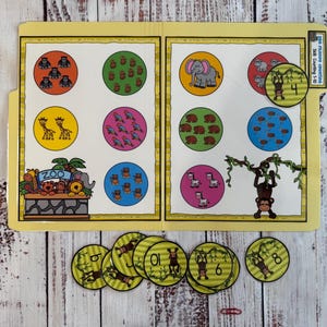 May include: A yellow educational counting game with animal illustrations. The game features circles with various animals and numbers, along with matching number cards. The illustrations include elephants, giraffes, monkeys, and other zoo animals. The game is designed for early childhood education.