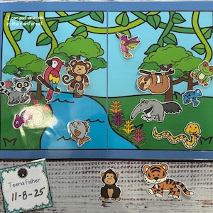 May include: A blue rainforest-themed learning board with various animal cutouts, including a monkey, parrot, and snake. The board has the text "I can put animals in the rainforest." Additional animal cutouts are placed below the board.