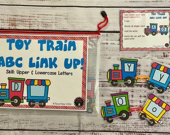 Può includere: Un set di treni giocattolo colorato con vagoni con le lettere e una carta di istruzioni. La carta dice "Posso abbinare le lettere maiuscole e minuscole". I vagoni sono rosso, blu, verde e giallo. Le lettere sui vagoni sono D, Y, O e Y. La carta di istruzioni dice "Treno Giocattolo ABC Link Up!" e "Abilità: Lettere Maiuscole e Minuscole".