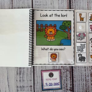 May include: An open spiral-bound children's book featuring a cartoon lion illustration with the text "Look at the lion!" and "What do you see?" Animal flashcards are visible. A small card with the name "Teena Fisher" and the date "9-20-2025" is also present.