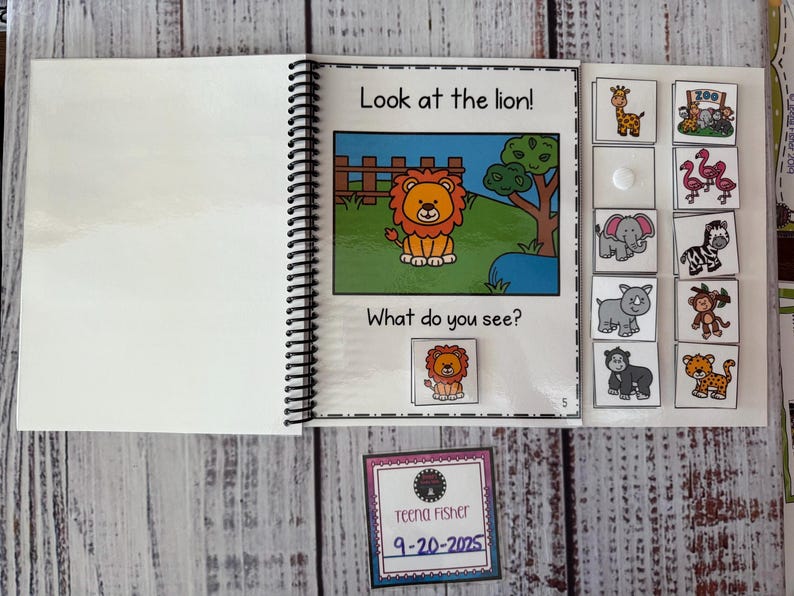 May include: An open spiral-bound children's book featuring a cartoon lion illustration with the text "Look at the lion!" and "What do you see?" Animal flashcards are visible. A small card with the name "Teena Fisher" and the date "9-20-2025" is also present.