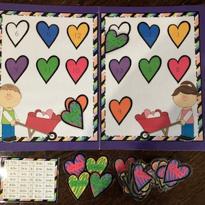 May include: A purple folder with a colorful heart-shaped design. The folder contains a set of educational flashcards with addition facts for young learners. The flashcards feature hearts with numbers and addition equations. The folder also includes a chart with addition facts.