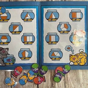 May include: A blue educational folder titled Fish Fractions with illustrations of fish bowls containing geometric shapes divided into fractions. The folder features cartoon cats and includes loose fish-shaped cutouts labeled with fractions like 1/2 and 1/3.