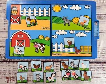 Può includere: Un puzzle blu illustrato a tema fattoria con quattro sezioni etichettate Cavalli, Capre, Polli e Mucche. Ogni sezione ha un pezzo di puzzle corrispondente. I pezzi del puzzle sono sparsi sotto il tabellone principale. Il testo "Animal Sort" è visibile.