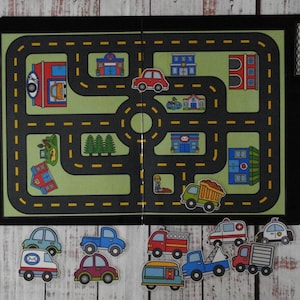 May include: A black folder containing a green play mat with a printed black road network, yellow dashed lines, and various buildings. Includes several detachable vehicle cutouts such as cars, trucks, an ambulance, and a tow truck for interactive play.