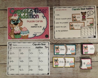 May include: A set of printable educational worksheets and puzzle pieces featuring a cartoon bear holding cupcakes. The worksheets include addition problems for numbers up to 20. The puzzle pieces have addition problems and their answers. The text on the worksheets says "Cupcake Bear Addition".