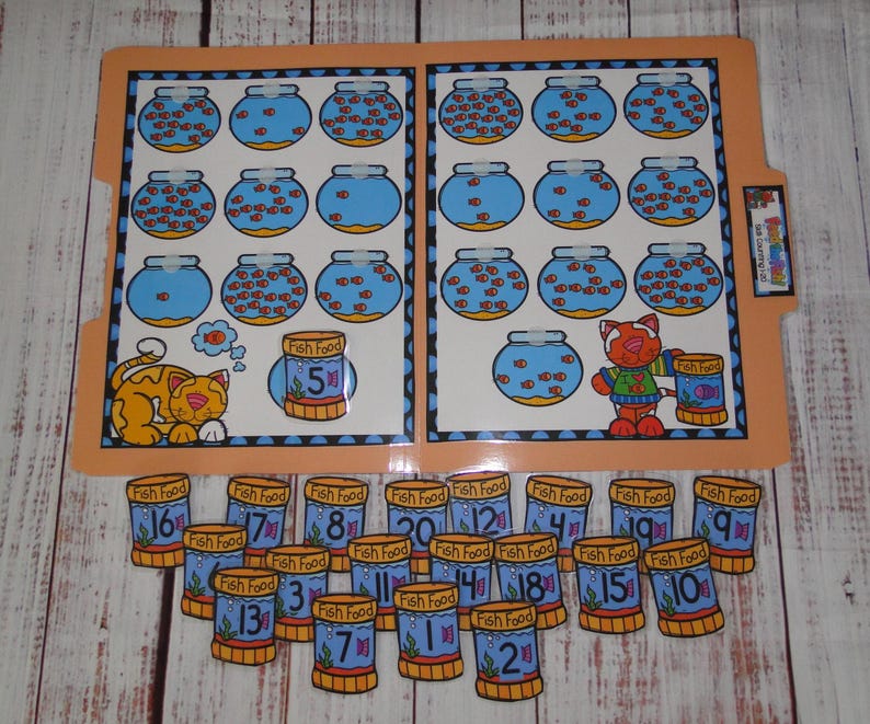 May include: A laminated file folder learning activity featuring illustrations of fish bowls with varying numbers of orange fish, a cat, and fish food containers. Includes loose cut-out fish food containers labelled with numbers 1 through 20.