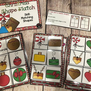 May include: A Christmas-themed shape matching game with cards featuring shapes like circles, rectangles, and hearts. The game includes a title card that reads "Christmas Shape Match" and instructions for matching shapes. The cards have a red and white border.