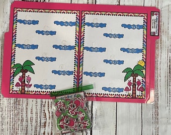 May include: A pink file folder with multiplication problems, palm trees, and flamingo illustrations. A small bag of flamingo-themed number cutouts is in front of the folder. The folder has the text "Flamingo Times Facts" on the tab.