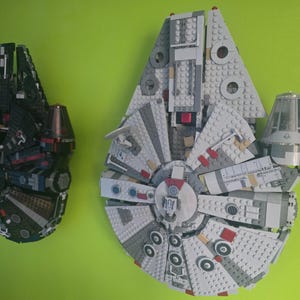 Könnte beinhalten: Zwei detaillierte LEGO-Modelle des Raumschiffs Millennium Falcon, eines in Schwarz und das andere in Grau und Weiß, werden vor einem grünen Hintergrund gezeigt. Die Modelle bestehen aus ineinandergreifenden Kunststoffbausteinen und weisen komplizierte Designs auf.