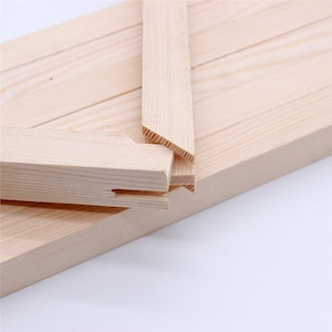 May include: Unfinished light-colored wooden stretcher bars for canvas framing. The set includes multiple rectangular wooden strips with mitered, angled ends designed to interlock at the corners, featuring visible wood grain and natural texture.