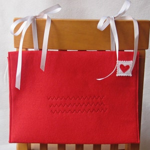 May include: Red felt chair pocket with white ribbon ties and a white felt heart on a red felt square.