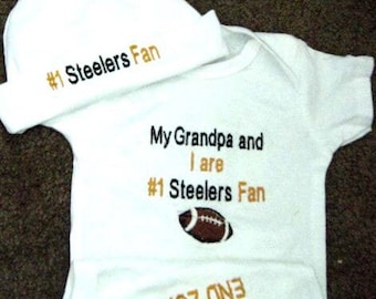 May include: White baby onesie with the text "My Grandpa and I are #1 Steelers Fan" and a football graphic. A white beanie with the text "#1 Steelers Fan" is also included.