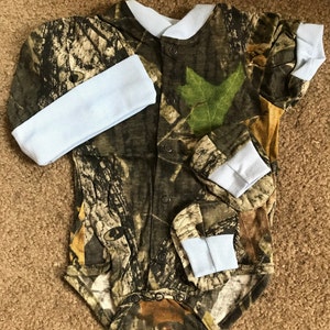 May include: Camouflage baby onesie with light blue trim and matching hat and booties.