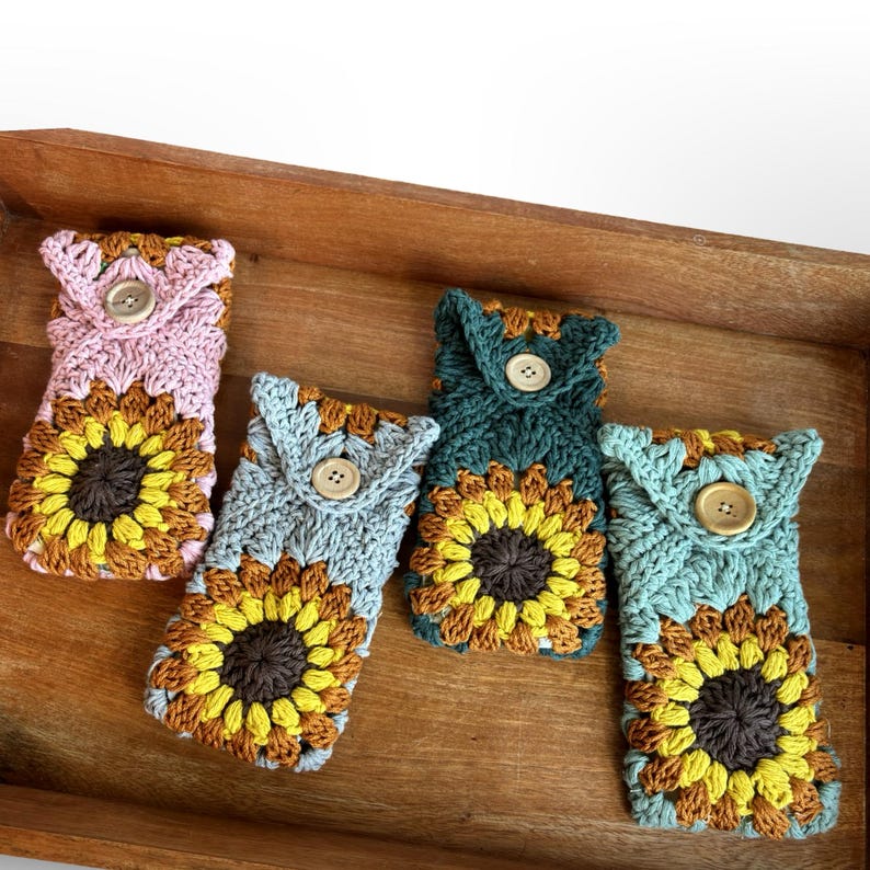May include: Four crocheted sunflower phone cases in pink, blue, green, and light blue with brown buttons.