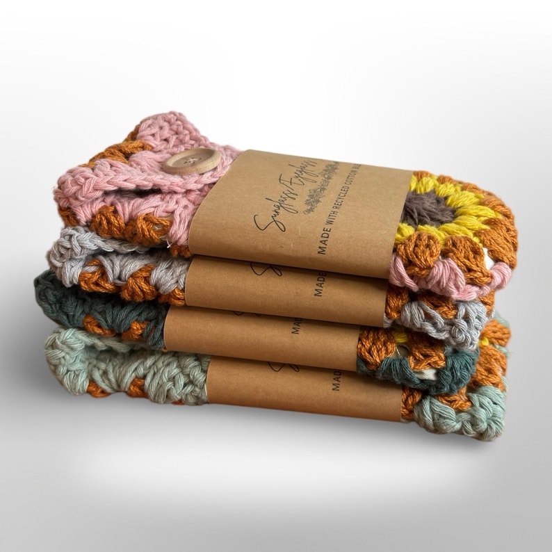 May include: A stack of four crocheted dishcloths in pink, gray, green, and orange with a sunflower design. The dishcloths are made with recycled cotton and have a brown paper label that says "Simply Earth Friendly" and "Made with Recycled Cotton".