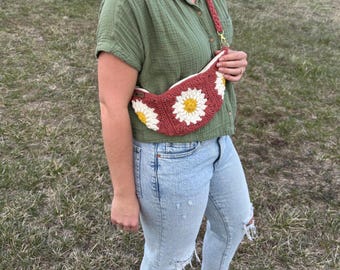 May include: A crocheted daisy flower-shaped bag with a red and white color scheme. The bag is worn as a crossbody bag and has a long strap.