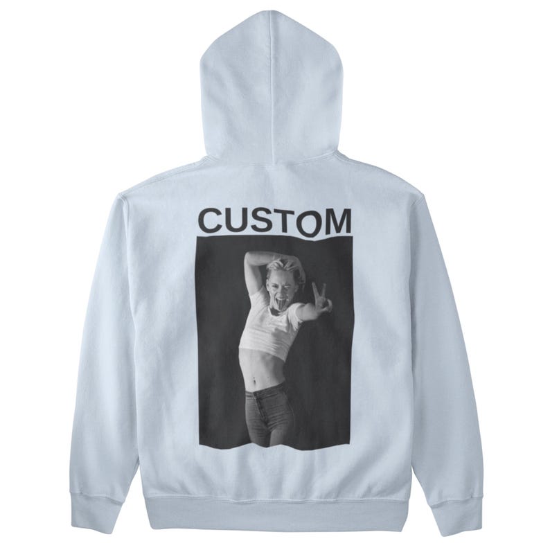 May include: A light blue hoodie with a black and white image of a person making a peace sign. The word "CUSTOM" is printed in black above the image. The hoodie has a hood and long sleeves.