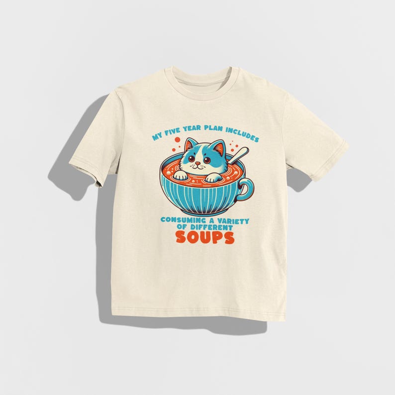 May include: A beige t-shirt featuring a cartoon cat in a bowl of soup. The text on the shirt reads "My five year plan includes consuming a variety of different soups."