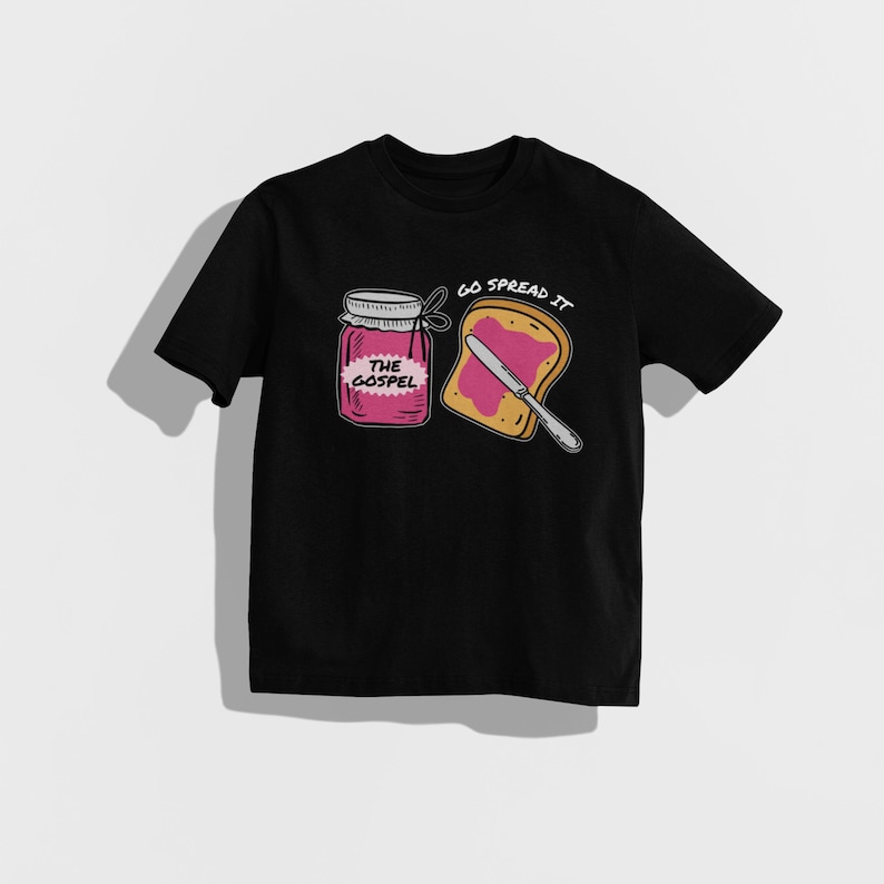 May include: Black t-shirt featuring a graphic of a jar labeled "The Gospel" and a slice of toast with jam and a knife. The text "Go Spread It" is above the toast. The design is in a cartoon style.