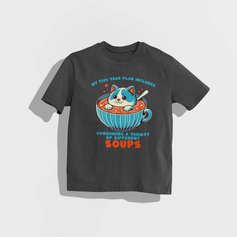 May include: A dark grey t-shirt featuring a cartoon cat in a bowl of soup. The text on the shirt reads "My five year plan includes consuming a variety of different soups."