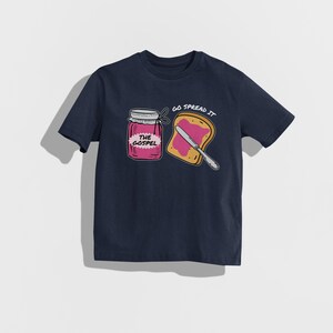 May include: Navy blue t-shirt featuring a graphic of a jar of jam labeled "The Gospel" and a slice of toast with jam and a knife. The text "Go Spread It" is above the toast. The design is in a cartoon style.