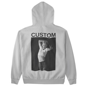 May include: White hoodie with a hood and a black and white image on the back. The image features a person making a peace sign and the word "CUSTOM" above the image.