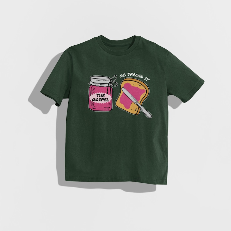 May include: Dark green t-shirt featuring a graphic of a jar labeled "THE GOSPEL" and a slice of toast with a knife, with the text "GO SPREAD IT". The design is in white, pink, and yellow.