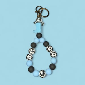 May include: A blue and white cow print beaded keychain with a blue boot charm and a gold key ring.