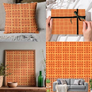 Op de afbeelding: Een decoratief kussen, een ingelijst kunstwerk en een geschenkdoos met een herhalend patroon van oranje en roestkleurige bloemvormen op een lichtoranje achtergrond. De geschenkdoos is vastgebonden met een zwart lint.