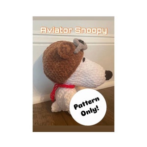 May include: Crocheted amigurumi pattern for a white dog wearing a brown aviator hat with a gray propeller. The pattern is for a plush toy and the image includes the text "Pattern Only!"