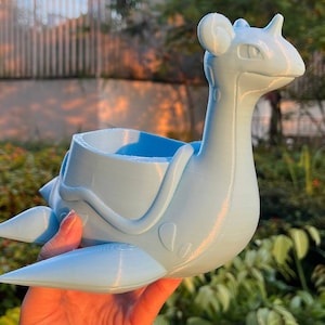 Op de afbeelding: Een lichtblauwe 3D-geprinte plantenpot in de vorm van een Pokémon-personage. De pot heeft een grote opening aan de bovenkant om te planten.