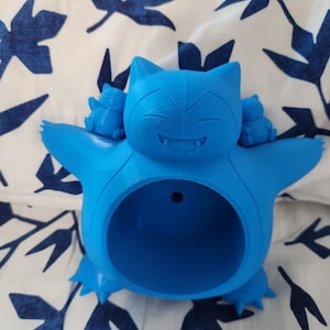 May include: A blue 3D printed planter shaped like a Pokemon character. The planter has a hole in the back for hanging and two smaller Pokemon characters on its back.