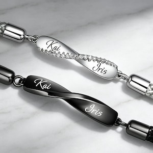 Könnte beinhalten: Zwei geflochtene Armbänder mit gedrehten Metallmittelteilen. Eines ist silberfarben mit eingelassenen klaren Steinen und den eingravierten Namen Kai und Iris. Das andere ist aus schwarzem Metall mit denselben Namen in Schreibschrift.