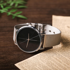 May include: A silver watch with a black face and a silver mesh band. The watch has a simple design with a single hand and no numbers.