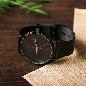 May include: A black wristwatch with a black mesh band and a round black face. The watch has a simple design with a thin silver hour and minute hand.