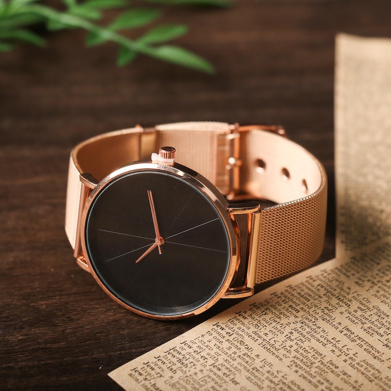 May include: A rose gold watch with a black face and a mesh band.