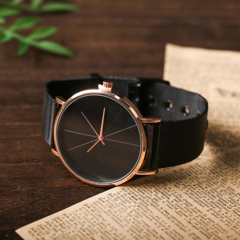 May include: A black and rose gold wristwatch with a black mesh band. The watch face is black with rose gold hands and markers.