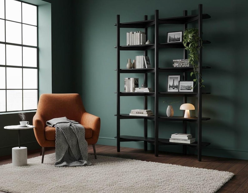 Lifestyle image of the black Wenge bookshelf in a moody, dark green room, styled with books and decor next to an orange armchair.