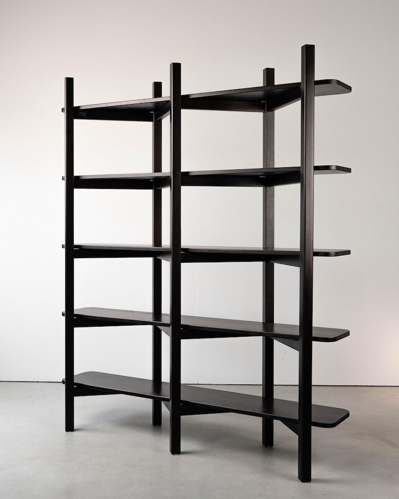 May include: A tall, black wooden bookshelf with five shelves. The shelves are supported by vertical posts and horizontal supports. The design is minimalist and modern, with a focus on clean lines and functionality. The bookshelf is freestanding.