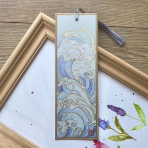 May include: A blue and gold bookmark with a wave design. The bookmark is made of paper and has a tassel.