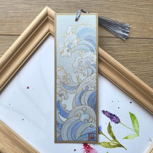 May include: A blue and gold bookmark with a wave design. The bookmark has a tassel and a red stamp with Japanese characters.