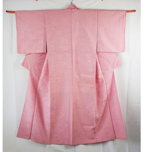 May include: A pink kimono with a subtle white floral pattern. The kimono is hanging on a wooden hanger against a white background.