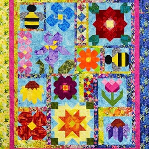 May include: A colorful quilt with a patchwork design featuring bees, flowers, and stars. The quilt is made up of various fabrics in shades of red, yellow, blue, green, and purple.