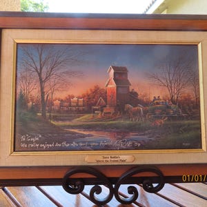 May include: Framed landscape painting titled "Above the Frosted Plain" by Terry Redlin. The artwork depicts a rural scene with a red barn, horses pulling a carriage, and a dog. The frame is a combination of dark and light brown wood.