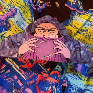 May include: Purple and pink plastic hair clip with a cartoon image of a wizard holding a purple orb. The wizard has a long white beard and a purple robe.